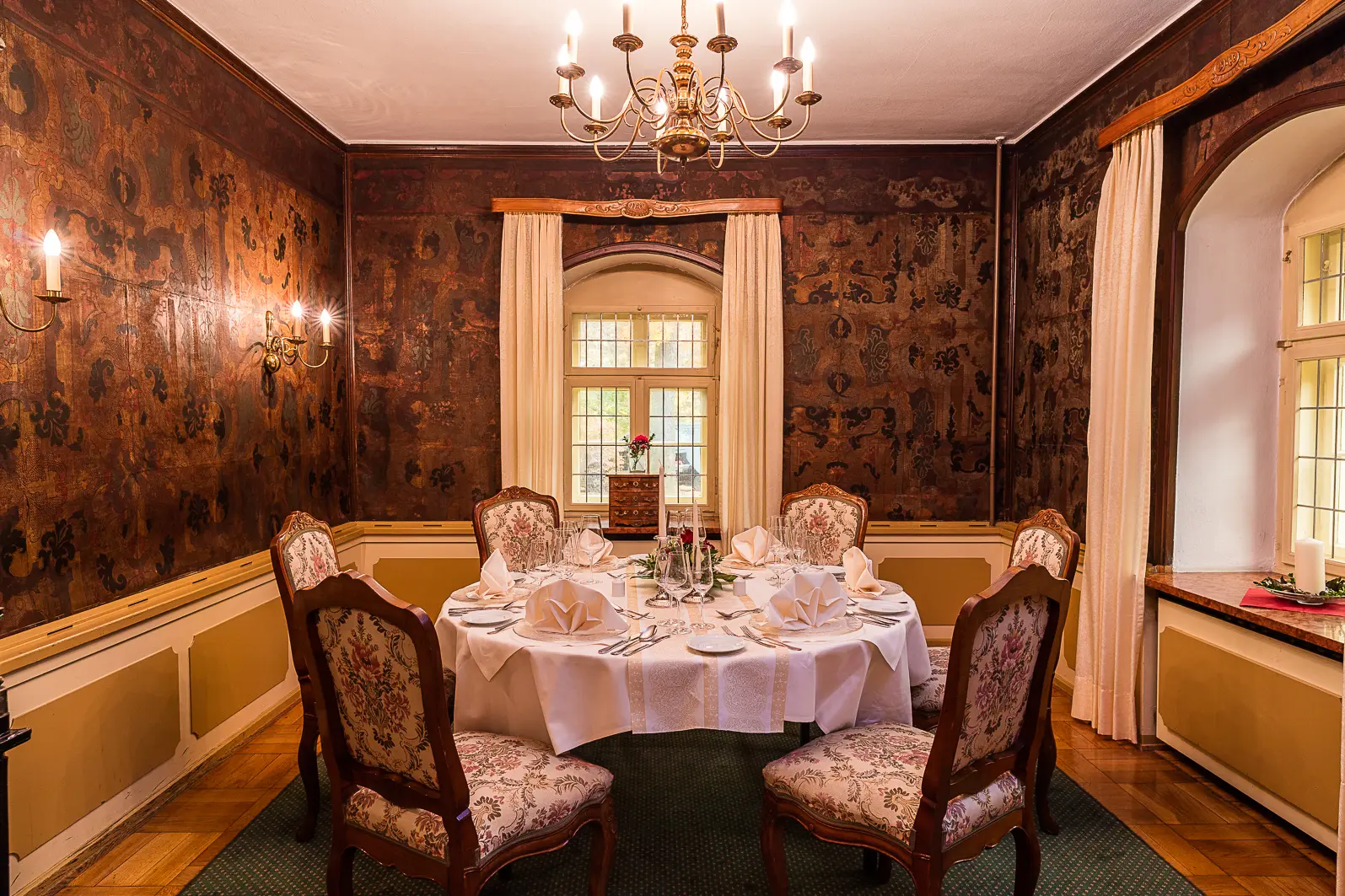 Elegantes Esszimmer mit rundem, festlich gedecktem Tisch und fünf gepolsterten Stühlen vor dunklen, ornamentalen Wänden.