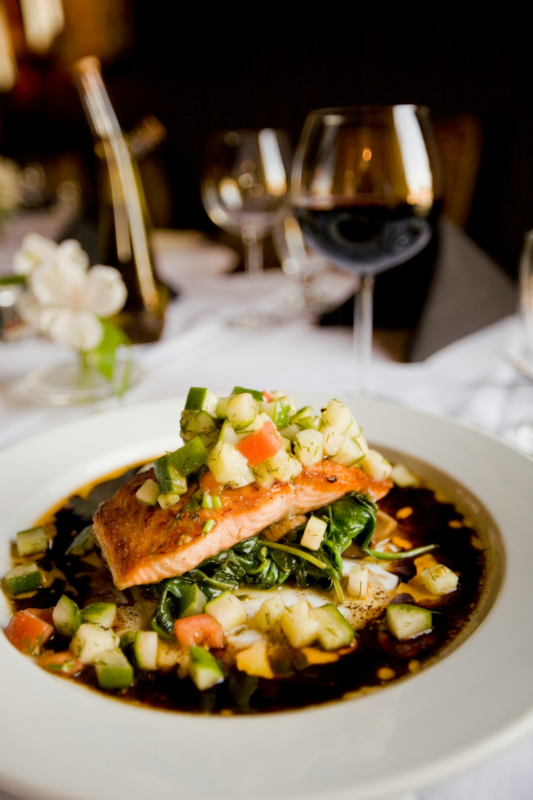 Gericht mit Lachs und buntem Gemüse auf Spinat in aromatischer Sauce, stilvoll angerichtet auf weiß gedecktem Tisch.