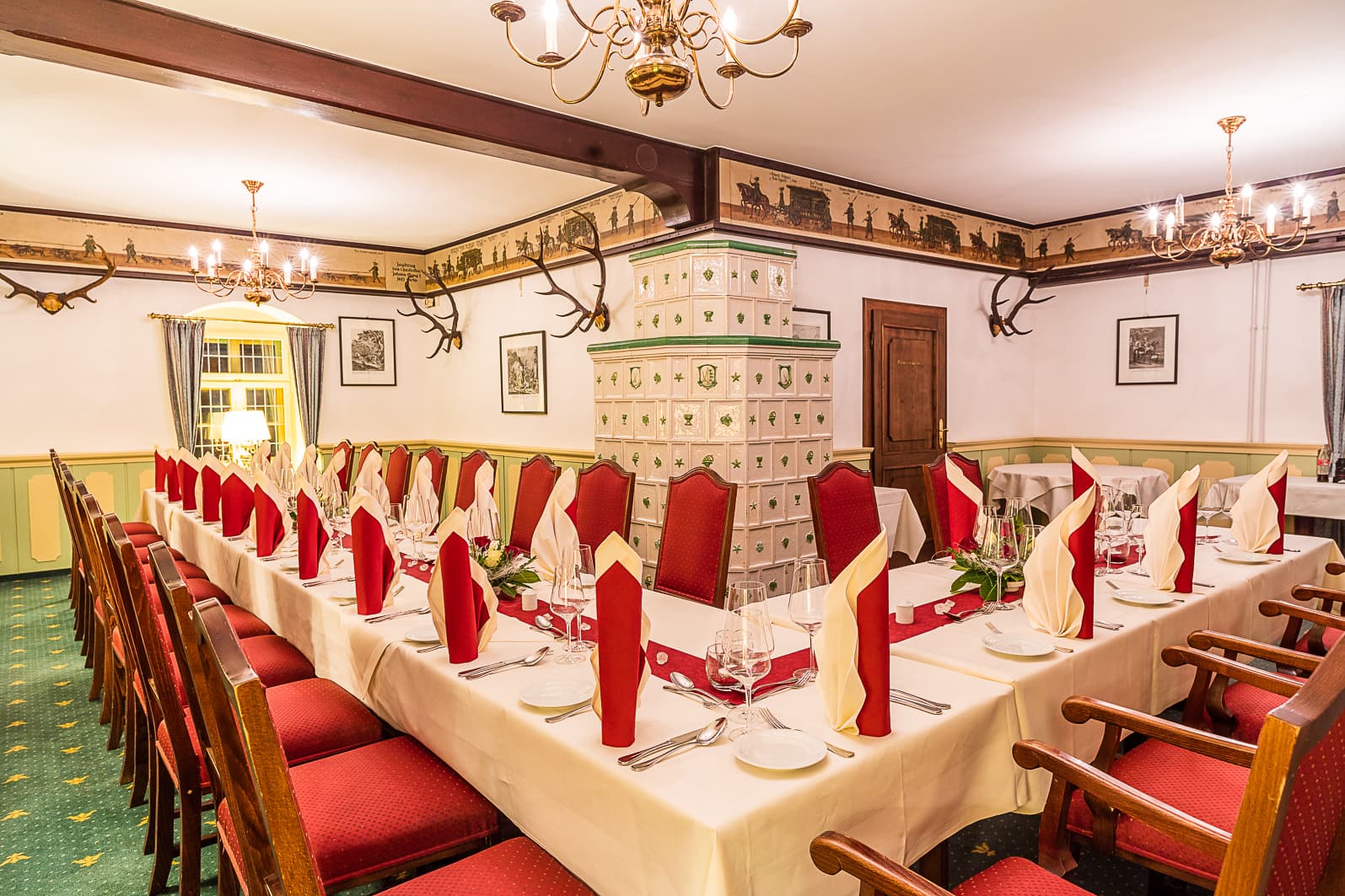 Churfuerstenzimmer Bright, rustic dining room of the Waldschänke Moritzburg with a covered table, tiled stove and wall decorations with hunting motifs.