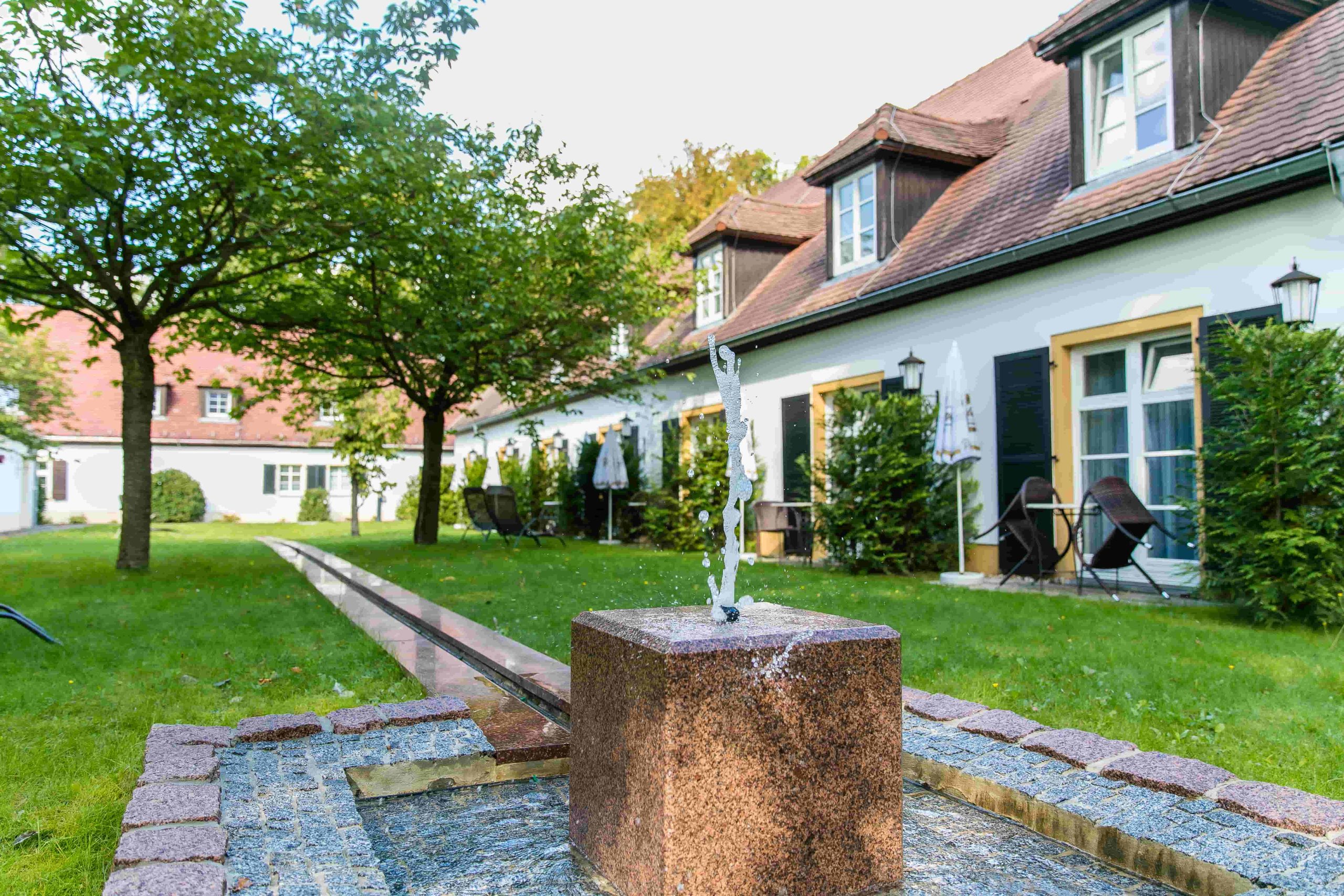 Blick auf den begrünten Innenhof der Waldschänke Moritzburg mit kleinem Steinbrunnen im Vordergrund.