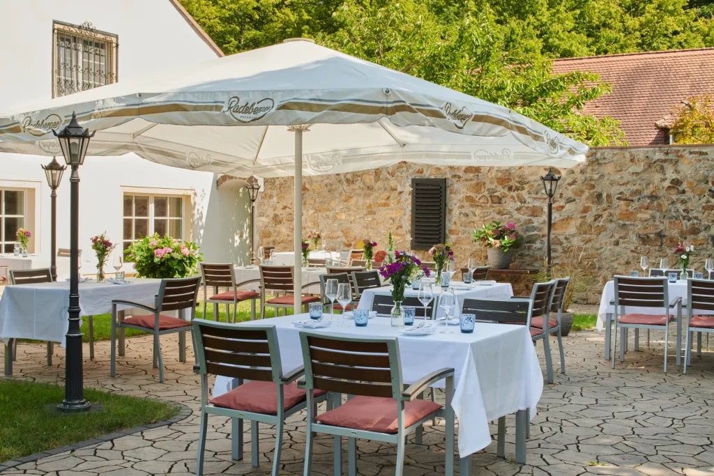 Eingedeckte Tische mit Blumen unter Sonnenschirmen am Grillplatz der Churfürstlichen Waldschänke Moritzburg vor Natursteinmauer