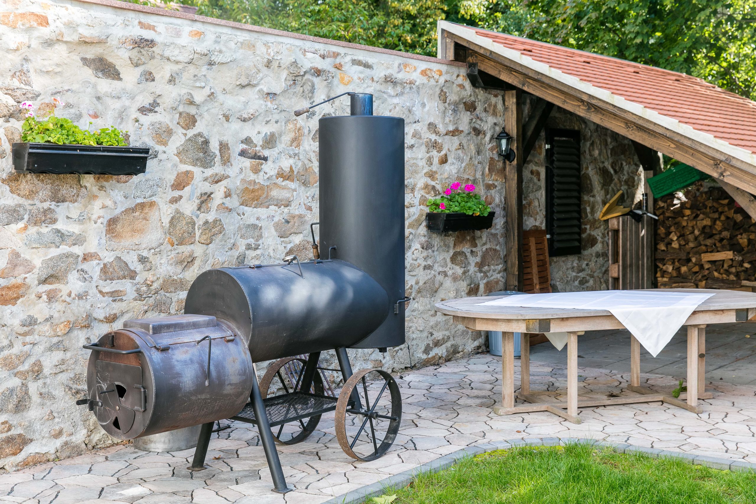 Grillplatz – Smoker-Grill & Sitzbereich Barbecue area with smoker grill on the natural stone wall and covered round table of the Churfürstliche Waldschänke Moritzburg