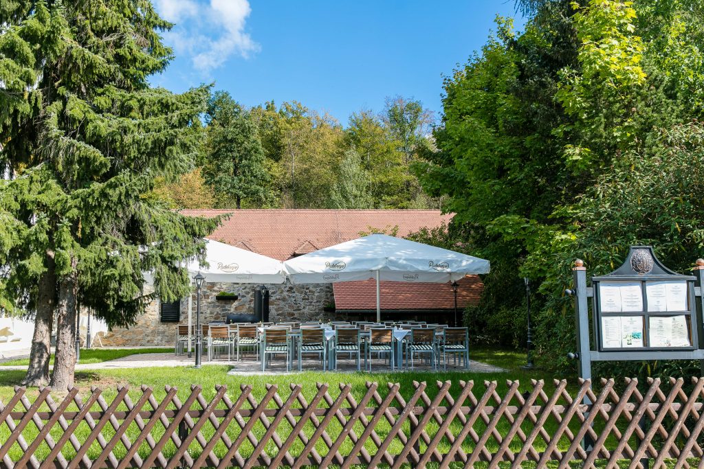 Grillplatz der Churfürstlichen Waldschänke Moritzburg mit Außensitzplätzen unter Sonnenschirmen vor Natursteinmauer im Grünen
