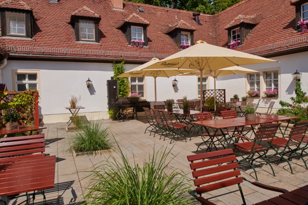 Innenhof der Churfürstlichen Waldschänke Moritzburg mit Biergarten-Sitzplätzen, großen Sonnenschirmen und Smoker-Grill an der historischen Fassade