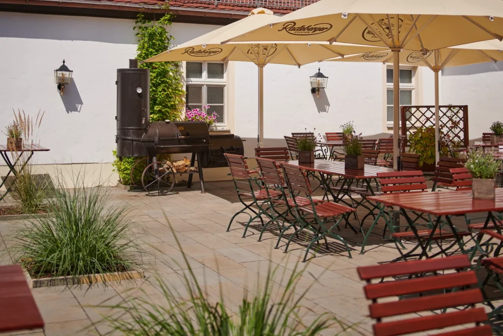 Innenhof der Churfürstlichen Waldschänke Moritzburg mit Biergarten-Sitzplätzen, Sonnenschirmen und Smoker-Grill an der historischen Fassade