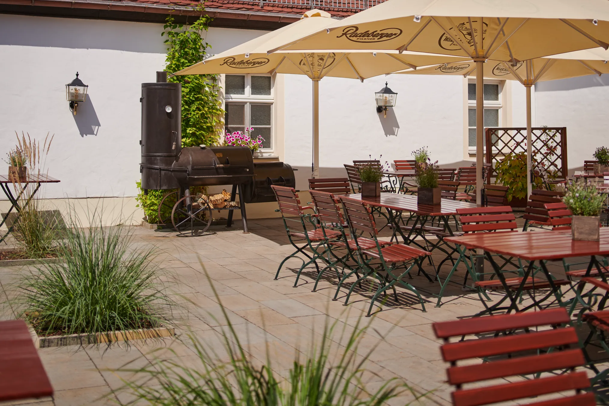 Innenhof – Biergarten mit Sonnenschirmen & Smoker-Grill Inner courtyard of the Churfürstliche Waldschänke Moritzburg with beer garden seating, parasols and smoker grill on the historic façade