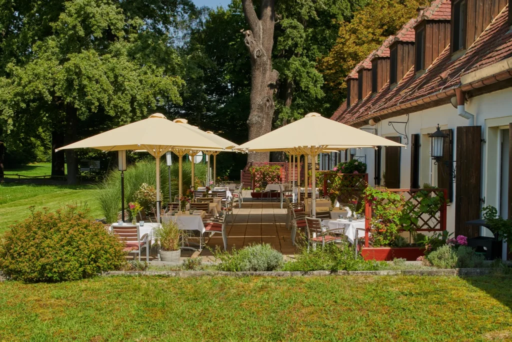 Wiesen-Terrasse der Churfürstlichen Waldschänke Moritzburg mit weiß eingedeckten Tischen unter Sonnenschirmen, Blick von der Rasenfläche auf die historische Fassade
