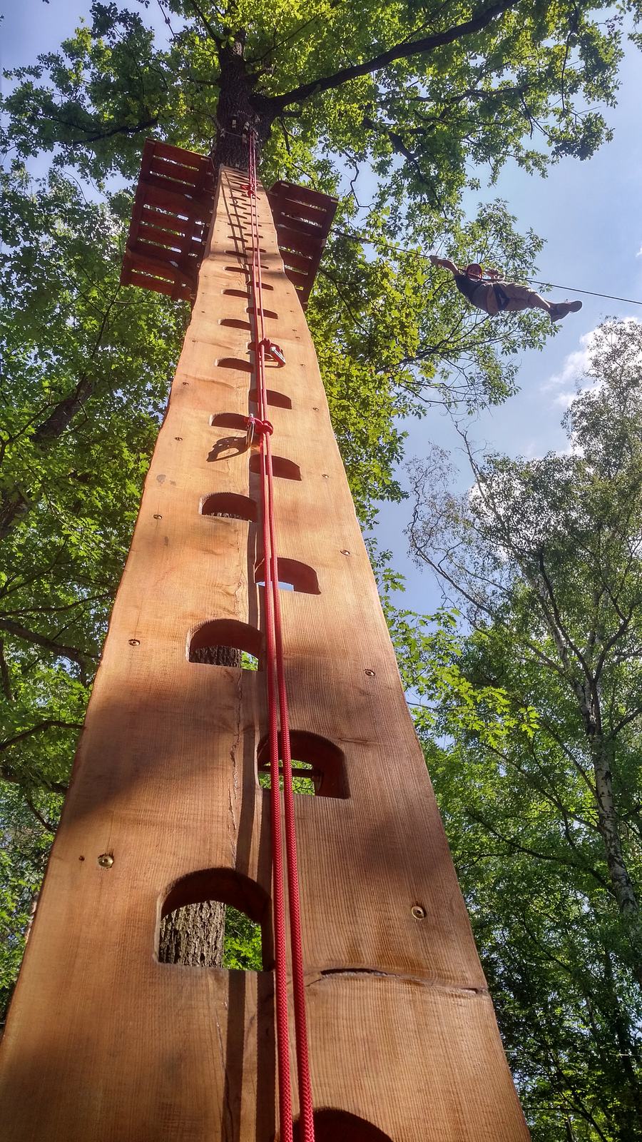 Aufstieg zum Seilbahnen-Parcours im Hochseilgarten Mittelteich Hoher Holzmast mit roter Strickleiter als Einstieg zum Seilbahnen-Parcours, im Hintergrund eine Person an der Seilbahn