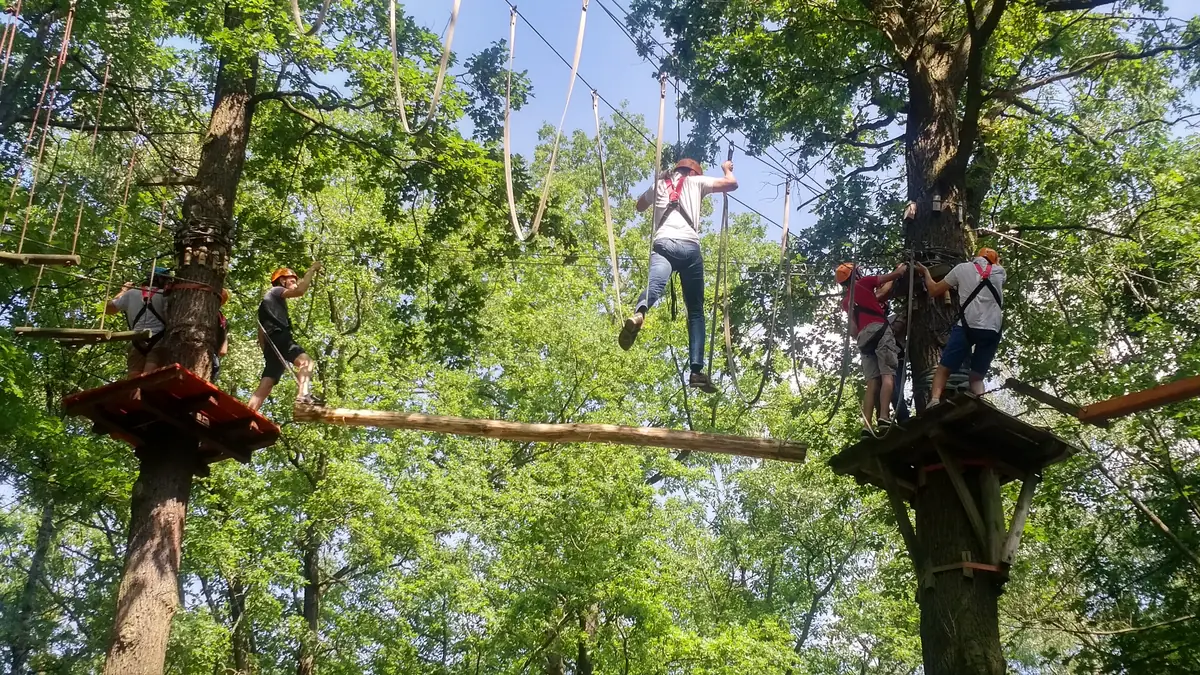 Balkenübergang im 10-Meter-Parcours Kletterin überquert einen freihängenden Holzbalken im 10-Meter-Parcours, weitere Teilnehmende warten auf den Plattformen